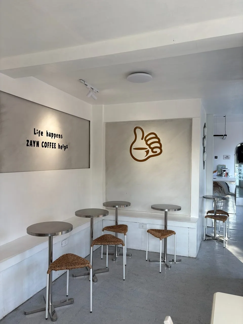 Bench seating and stools beneath a “Life happens, Zayn Coffee helps” wall sign